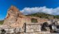 Carved marble blocks, columns, and ruined stone walls at ancient Ephesus beneath a bright blue sky