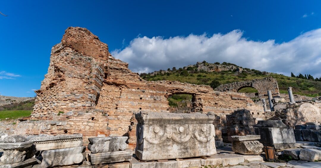 Carved marble blocks, columns, and ruined stone walls at ancient Ephesus beneath a bright blue sky