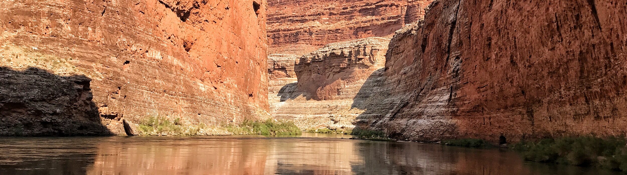 Grand Canyon cliffs reflected in the calm Colorado River beneath a bright blue sky