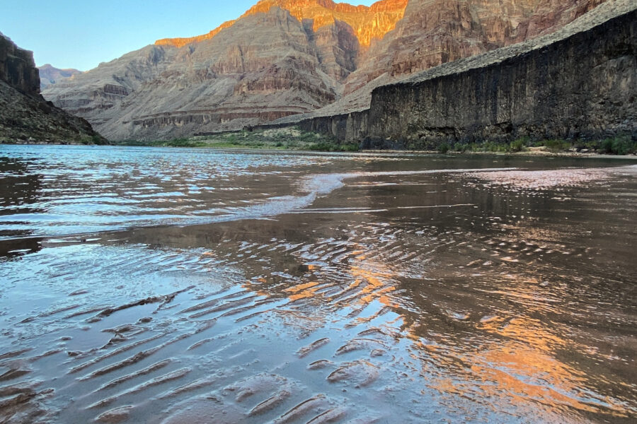 Early sunlight glowing on Grand Canyon cliffs above the Colorado River and rippled riverside sand