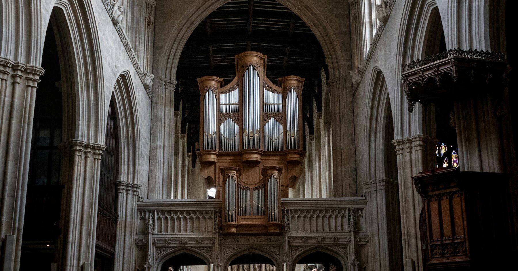 Historic English church interior with stone arches, timber ceiling, organ, and central aisle