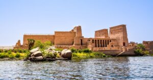 Ancient Philae Temple beside the Nile at Aswan with stone columns, river water, and desert hills