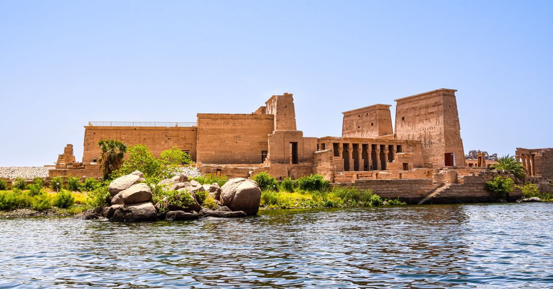 Ancient Philae Temple beside the Nile at Aswan with stone columns, river water, and desert hills